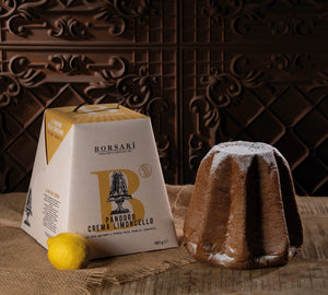 Borsari Panodoro Crema Limoncello cake packaging box shown next to a baked cake dusted with powdered sugar and a lemon on a rustic burlap surface against a dark carved wooden background.