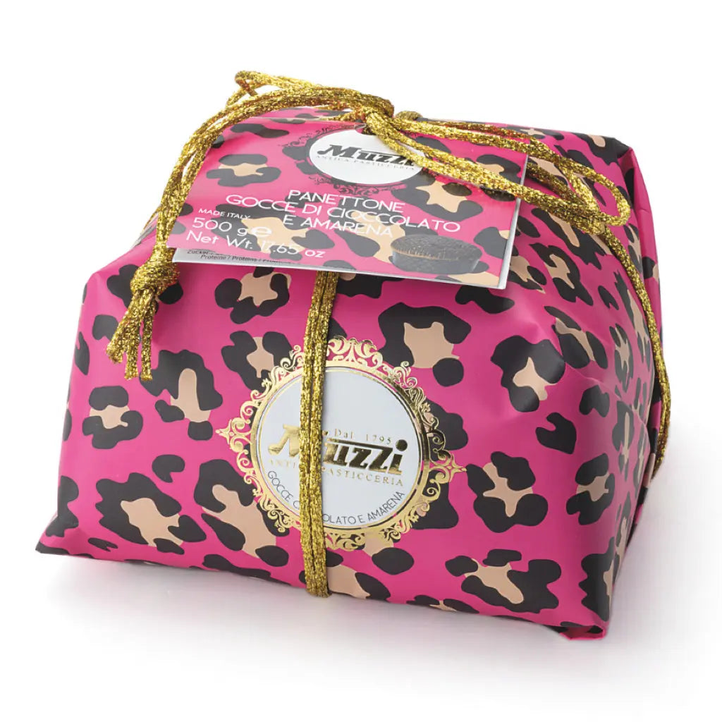 A panettone cake with black cherry and chocolate chips, wrapped in a pink and brown animal patterned paper, and a label that reads 'GOOD PANETTONE AWARD OF LOMBARDY'.