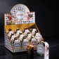 A retail display box filled with small Muzzi Panettonino Classic mini gift boxes, with one larger box standing in front on a dark reflective surface against a black background.