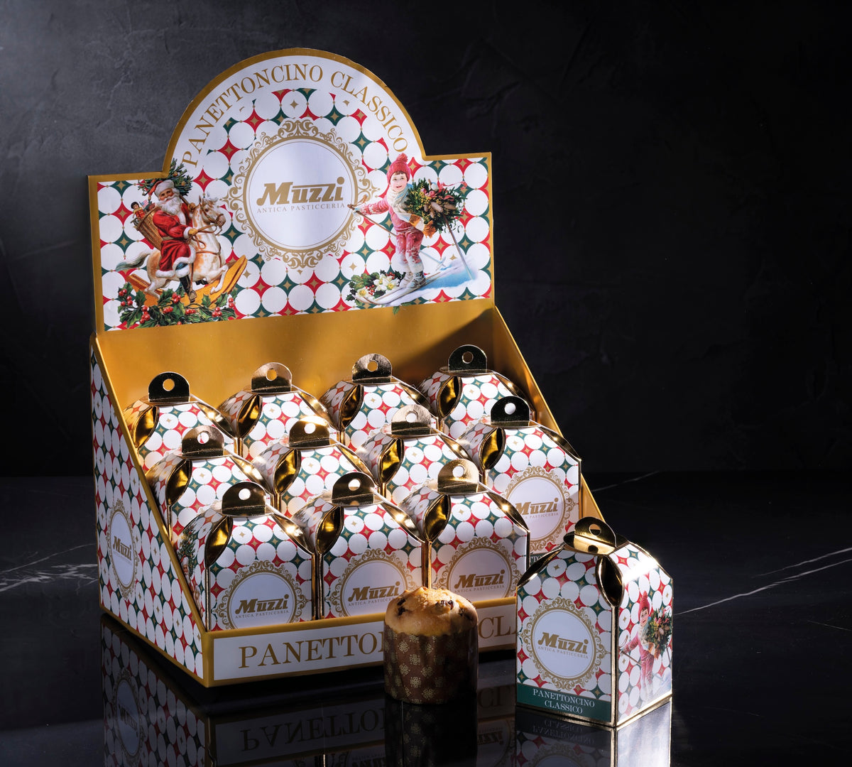 A retail display box filled with small Muzzi Panettonino Classic mini gift boxes, with one larger box standing in front on a dark reflective surface against a black background.