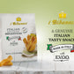 A bag of i Bibanesi Italian Mini Chunky Breadsticks stands on a white wooden surface with a few breadsticks placed in front. The packaging is white with gold and black text, and the background is a soft light green gradient.