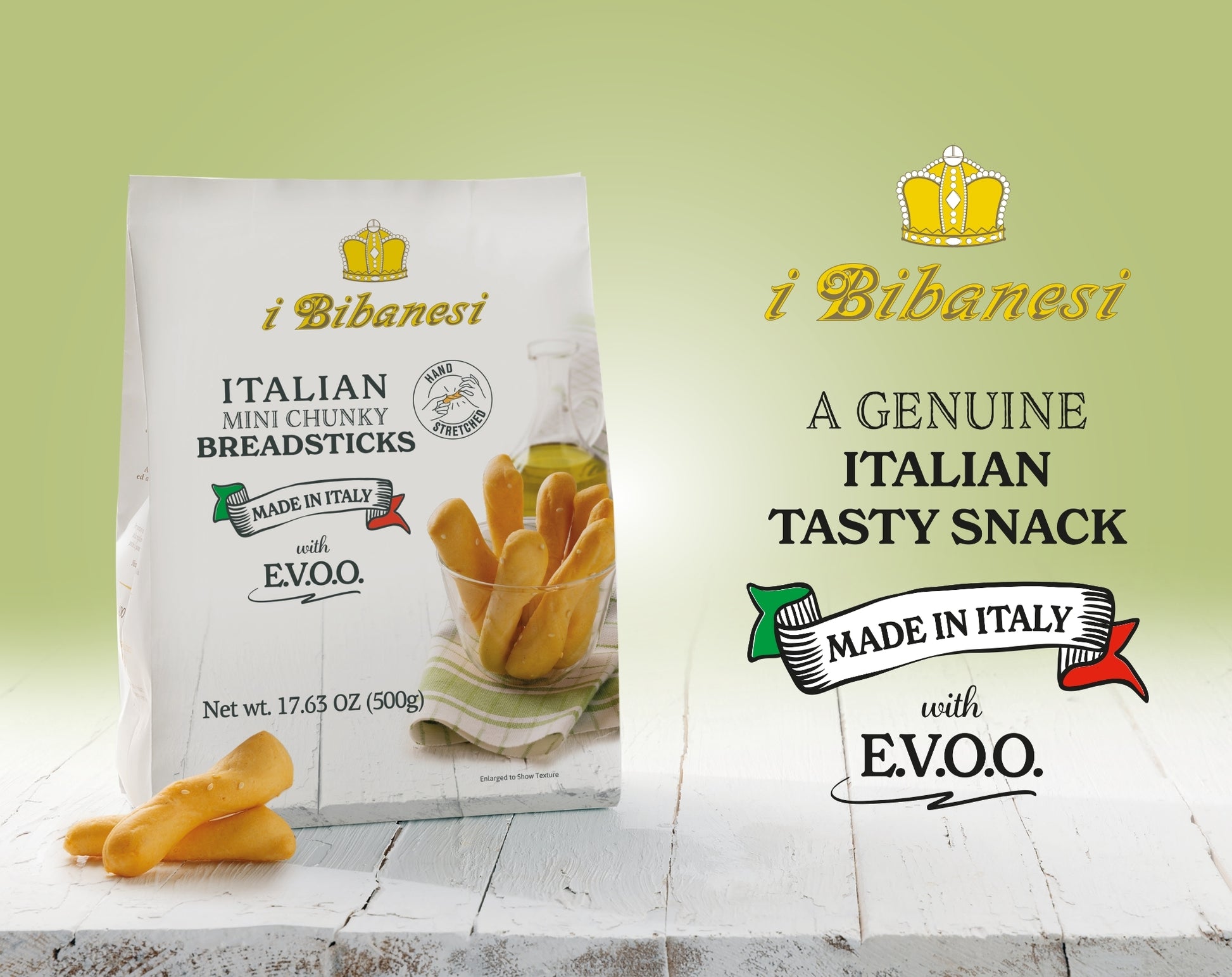 A bag of i Bibanesi Italian Mini Chunky Breadsticks stands on a white wooden surface with a few breadsticks placed in front. The packaging is white with gold and black text, and the background is a soft light green gradient.