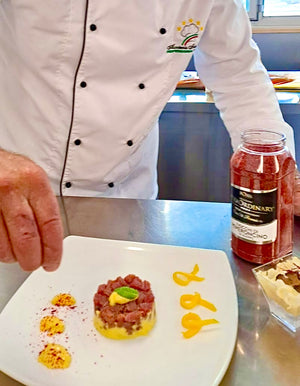 Chef preparing a dish with a bottle of red sauce on a kitchen counter with aleppo chili