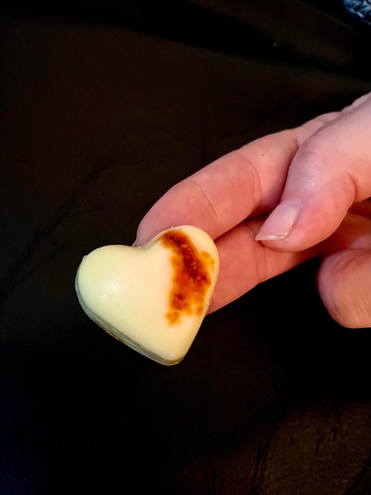 Heart-shaped cookie with a brown spot held in a hand against a dark background with aleppo chili flavor