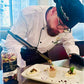 Chef preparing a dish in a kitchen with a bottle of Fracordinio on the counter with edible flowers on the top