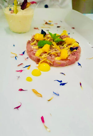 Tua tartare with yellow fruit compote and colorful edible flowers on the top and on a white surface