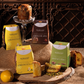 Four boxes of Roversi biscotti al forno are arranged on a rustic burlap-covered table with sliced biscotti pieces, whole lemons, and a glass pedestal holding a tall biscotti loaf. The boxes are yellow, brown, and green, labeled Limoncello, Cioccolato, and Pistacchio.