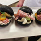 Three black buns with various fillings on a white plate.