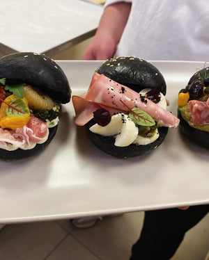 Three black buns with various fillings on a white plate.