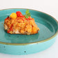 Casserole dish on a blue plate with yellow and red pepper drops on a white background