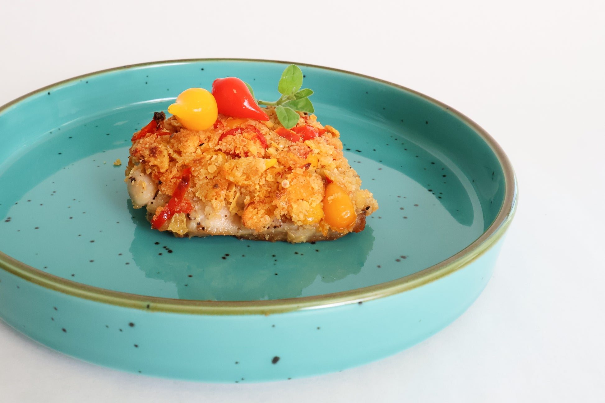 Casserole dish on a blue plate with yellow and red pepper drops on a white background