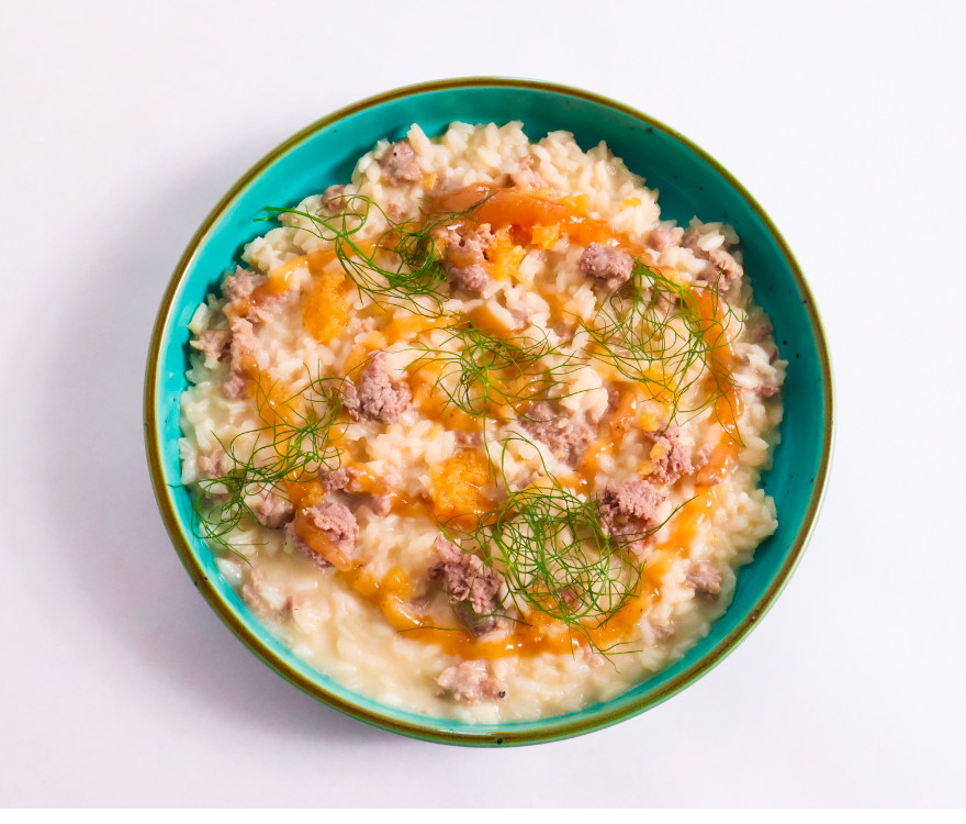 Risotto dish with sausage and herbs in a blue bowl on a white background
