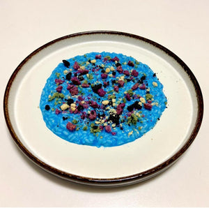 Blue risotto with colorful toppings on a white plate with brown rim