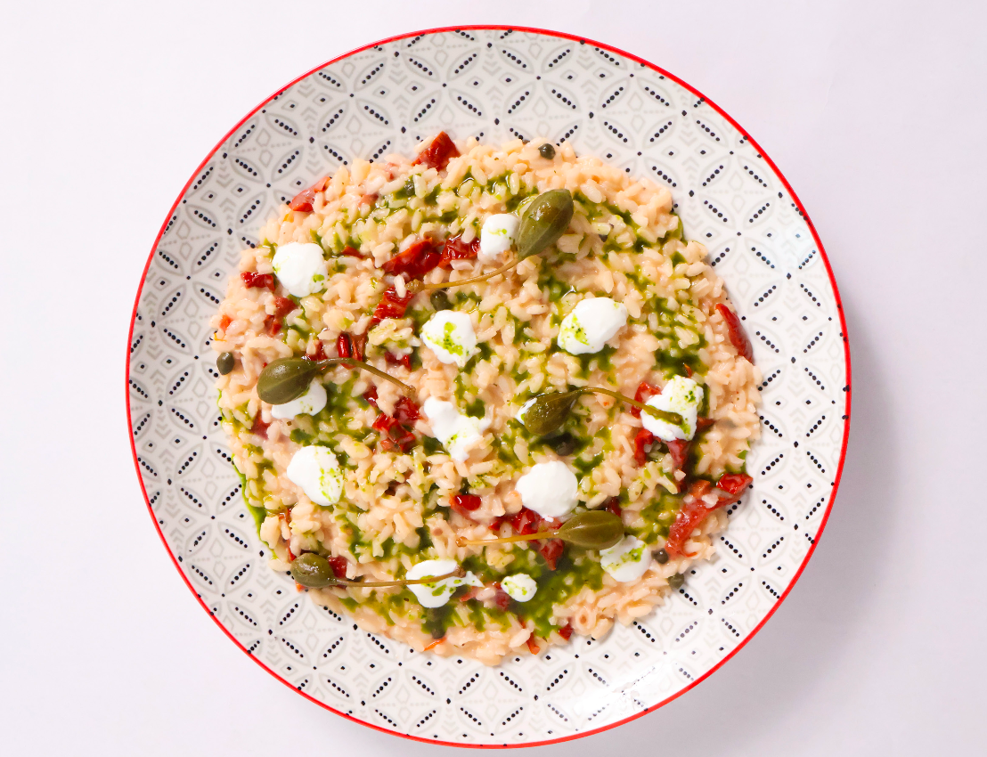 Plated dish of risotto with semi-dried tomatoes, capers and capers fruits on a white background