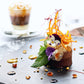 Delicate savory cake with floral garnishes, thin chili threads on a gray plate, accompanied by a glass of iced coffee.
