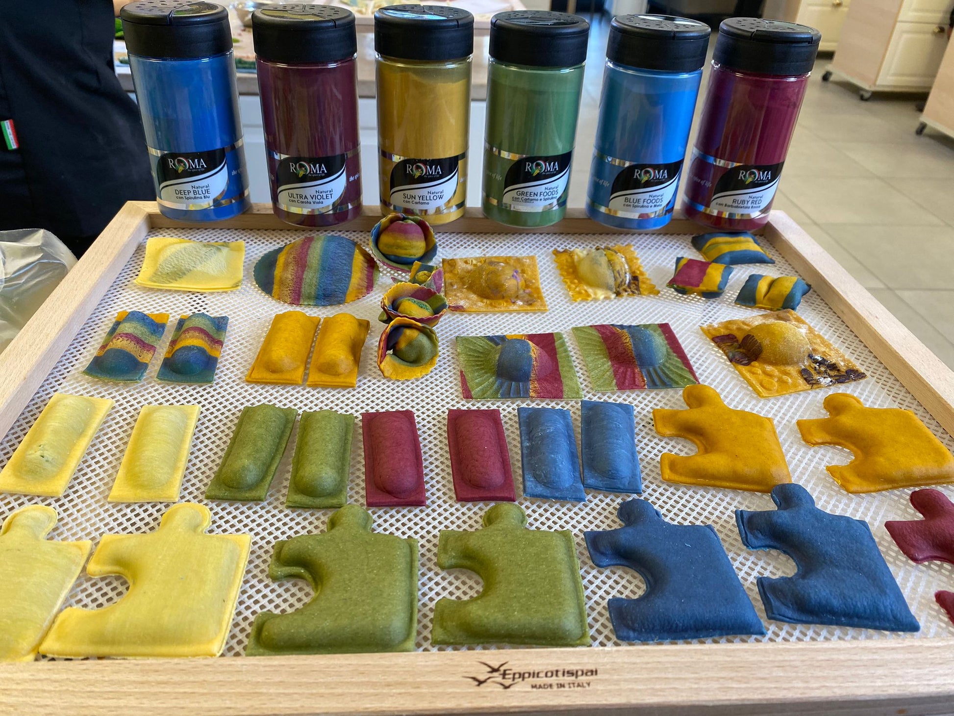 Colorful pasta shapes on a tray with paint colorfood jars in the background
