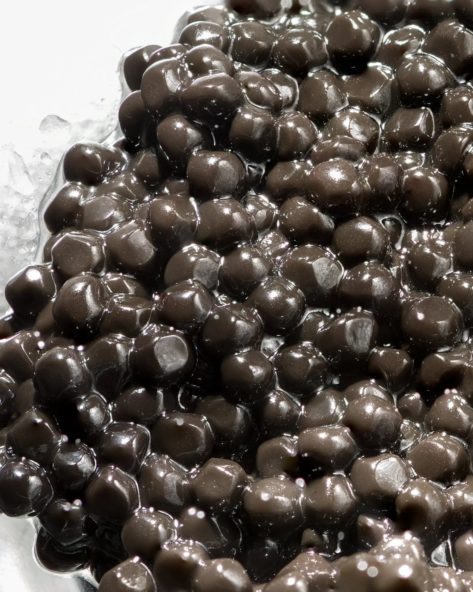 A close-up of glossy truffle pearls glistening with water, piled on a white surface.