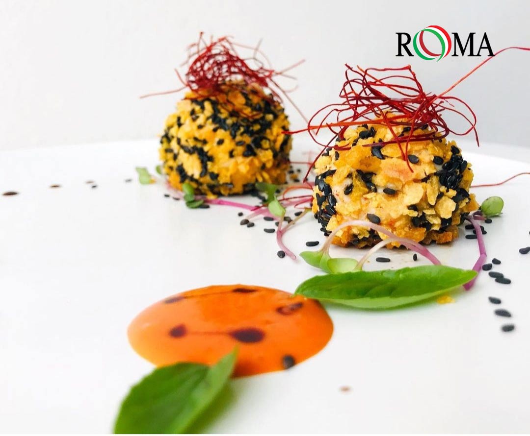 Two decorative rice balls on a white plate with 'ROMA' branding and thin chili threads on the top.