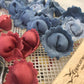 Red and blue rose-shaped ravioli on a textured surface with a wooden block in the foreground.