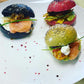 Three colorful buns with salmon and vegetables on a white plate.