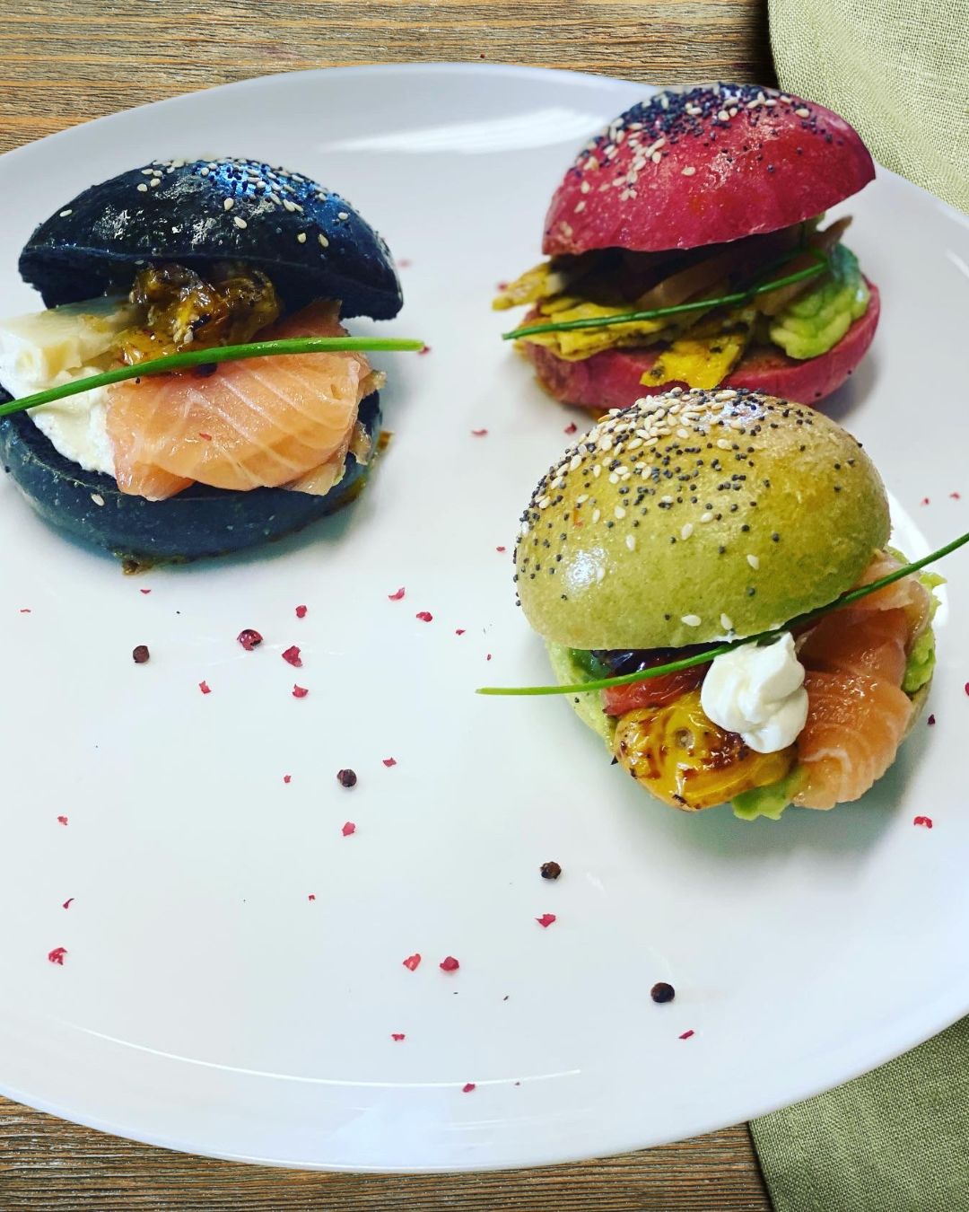 Three colorful buns with salmon and vegetables on a white plate.