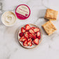 Bowl of strawberries, container of Vermont Crème Fraçè, and biscuits on a marble surface